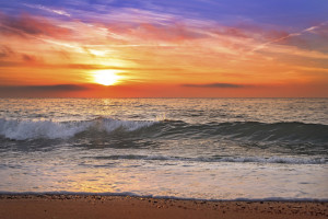 Colorful ocean beach sunrise with deep blue sky.