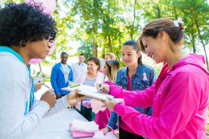 Diverse group of adults and teenagers are lined up at registration table in sunny park. 